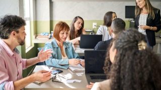 Adult students sitting at desk and talking in classroom with teacher